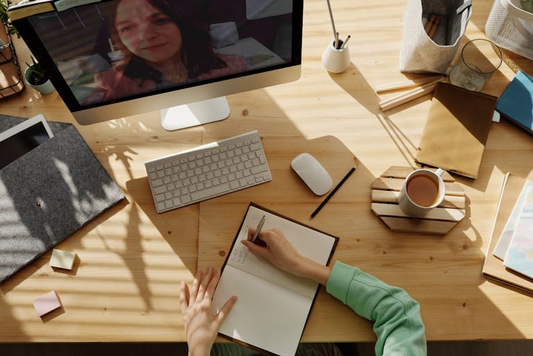 A student taking notes during a video call for online learning at home.
