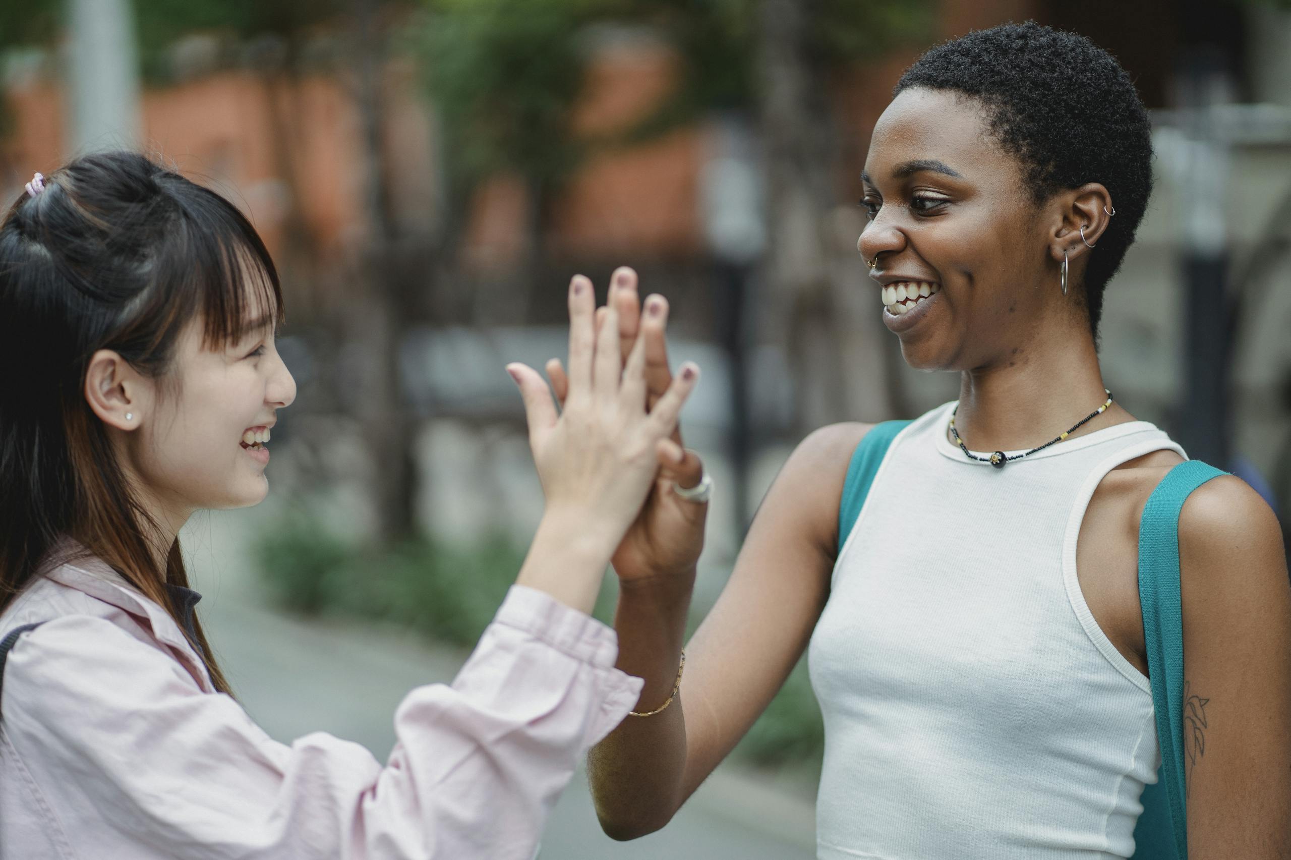 Two diverse friends sharing a joyful high five outdoors, promoting friendship and unity.